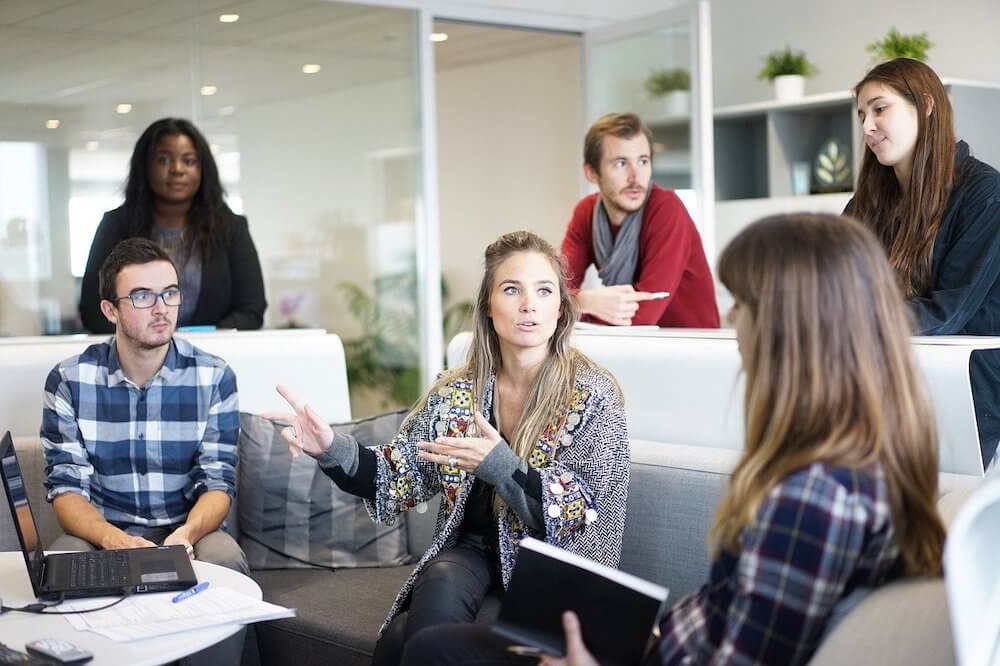 A photo with 6 people sitting in an office talking.